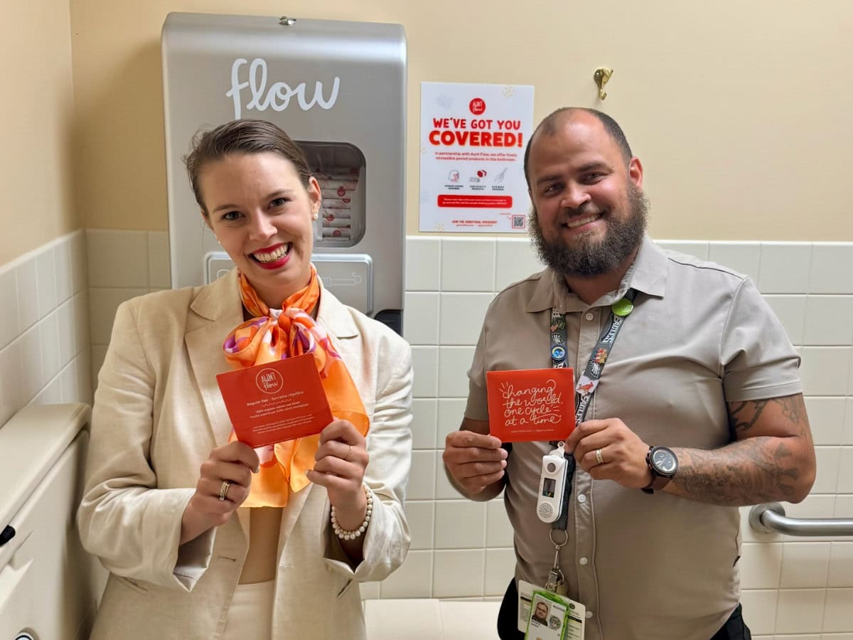 Two people holding coral pads and standing in front of an Aunt Flow dispenser