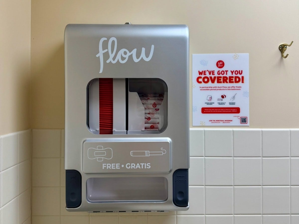 Aunt Flow Dispenser mounted on a tile wall with bathroom signage 